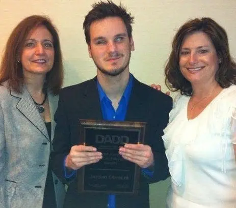 Jordan Obrecht holding a DADD award with two women.