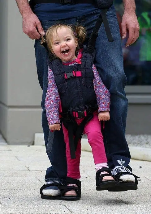Charlotte smiles in the Upsee, strapped to an adult.