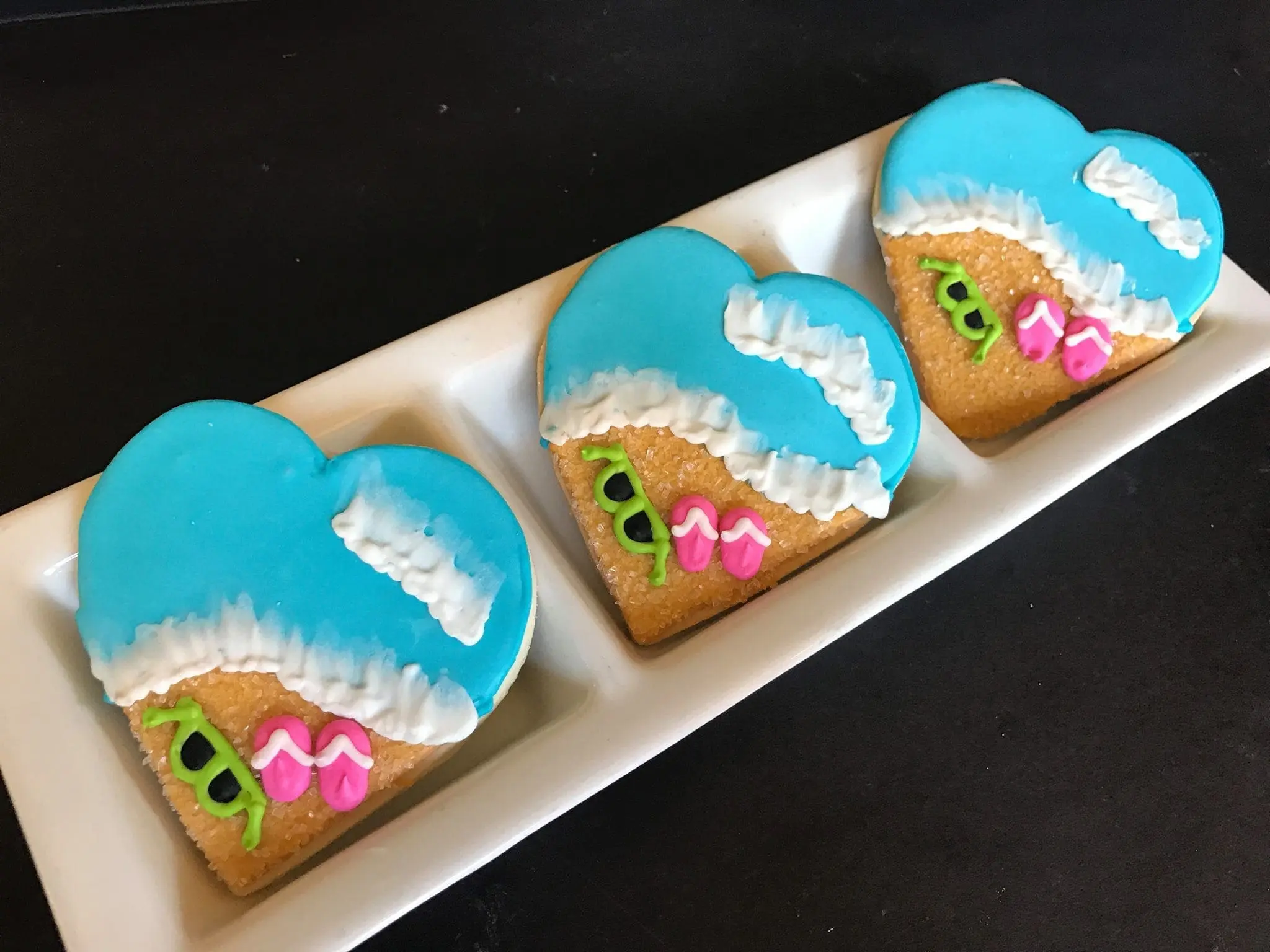Three heart-shaped cookies decorated as beach scenes on a white platter.