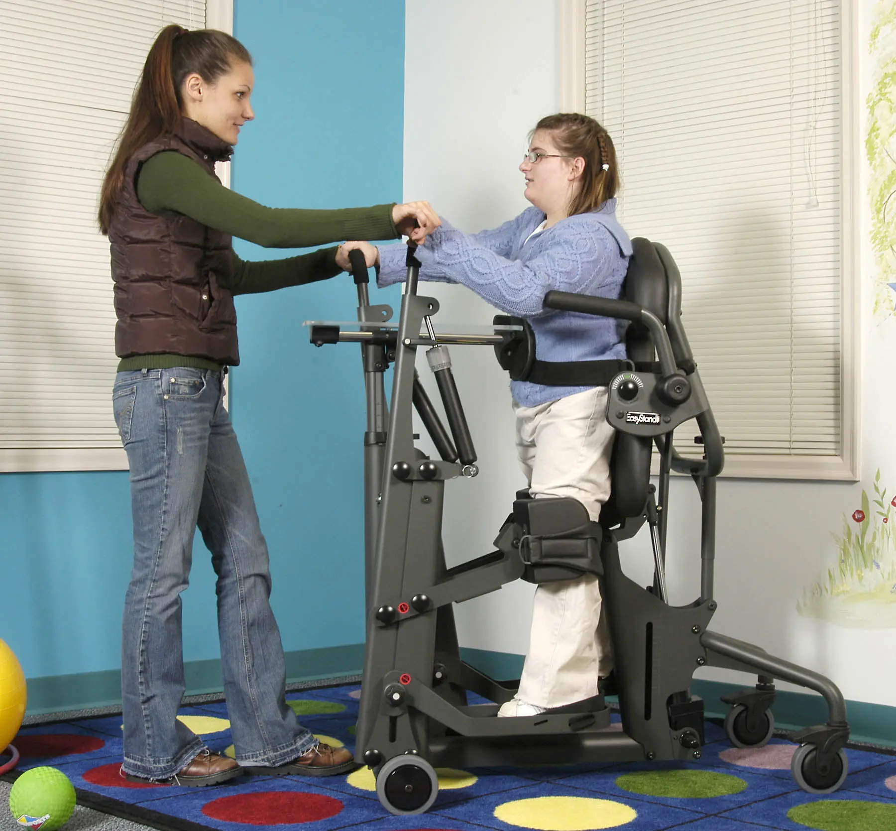 A young girl stands in a EvolvYouthGlider while a therapist assists her.