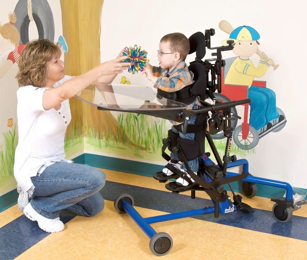 Woman reaches out to a child in a standing frame with a toy.