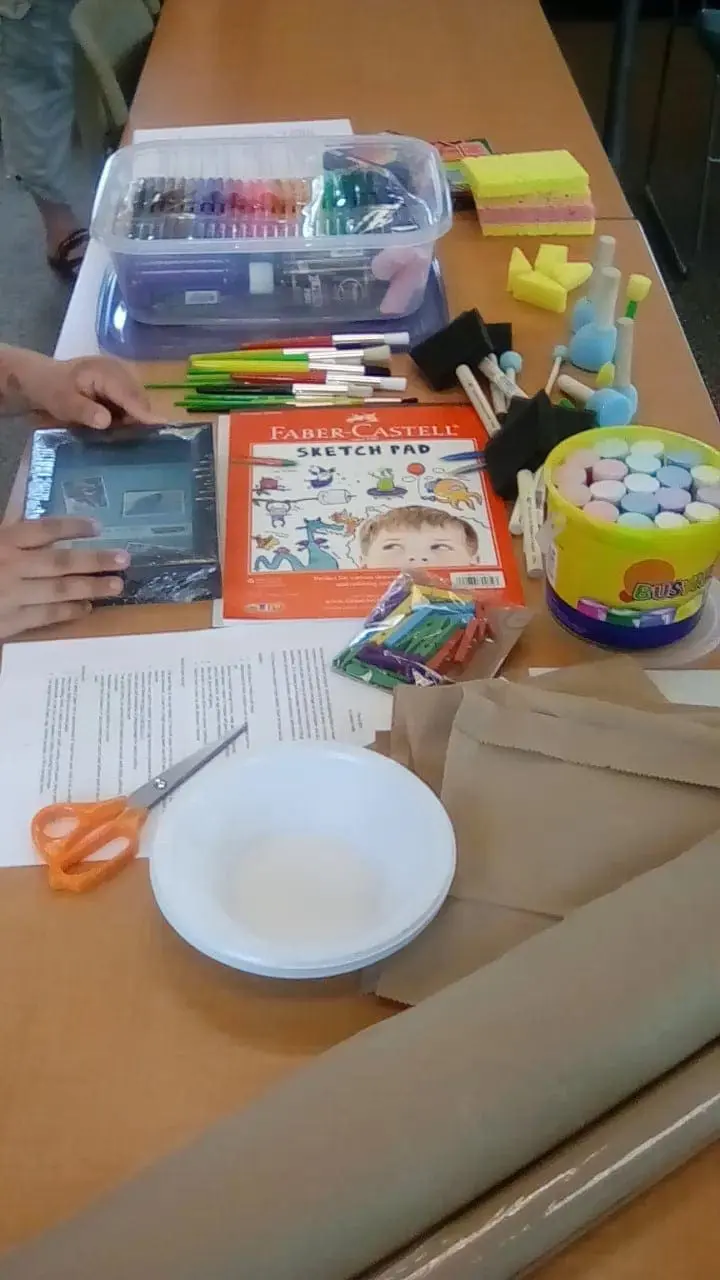 Art supplies including paint, markers, brushes, and paper are laid out on a table.