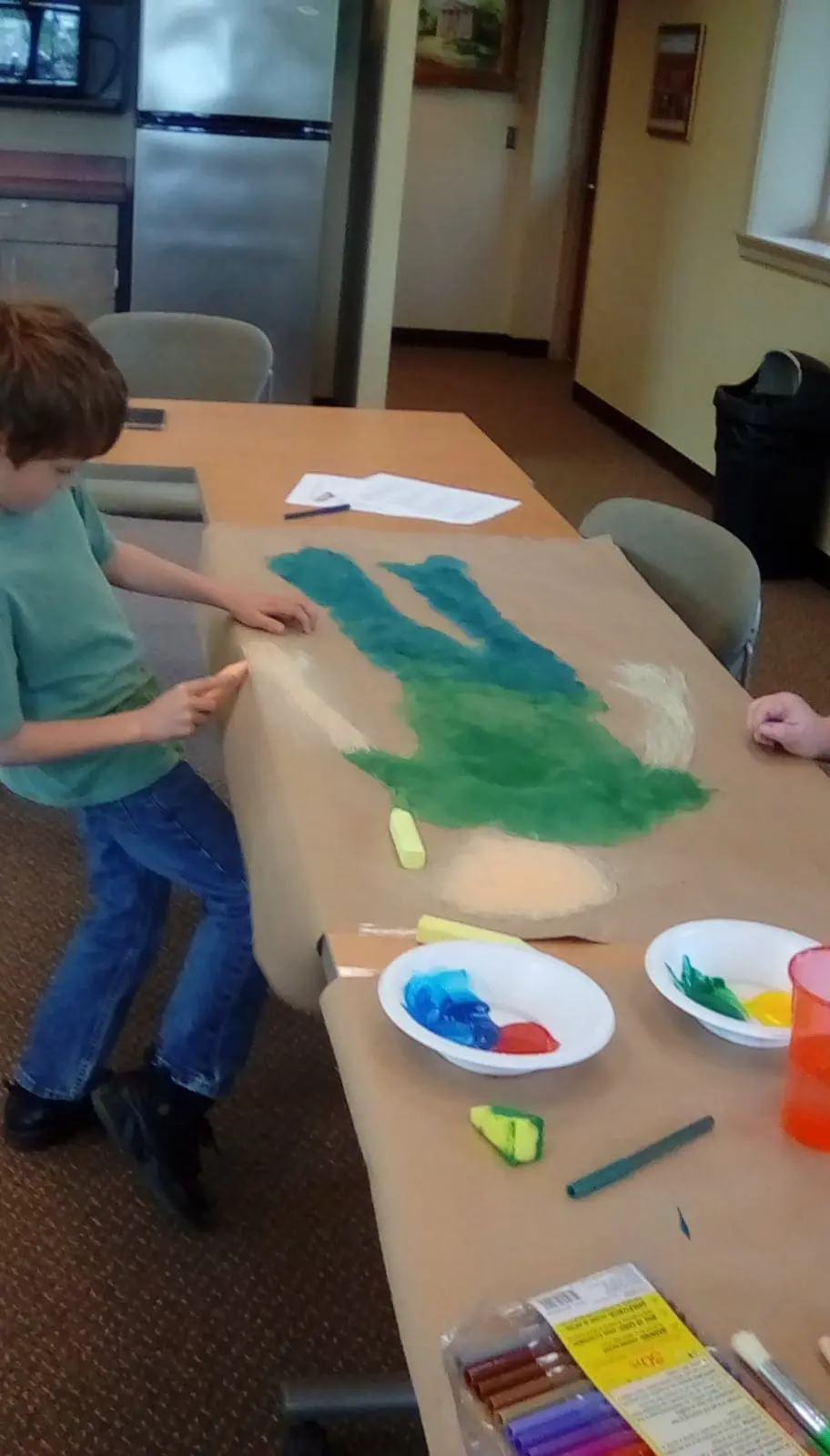 Charlie paints on large paper with green and blue colors.