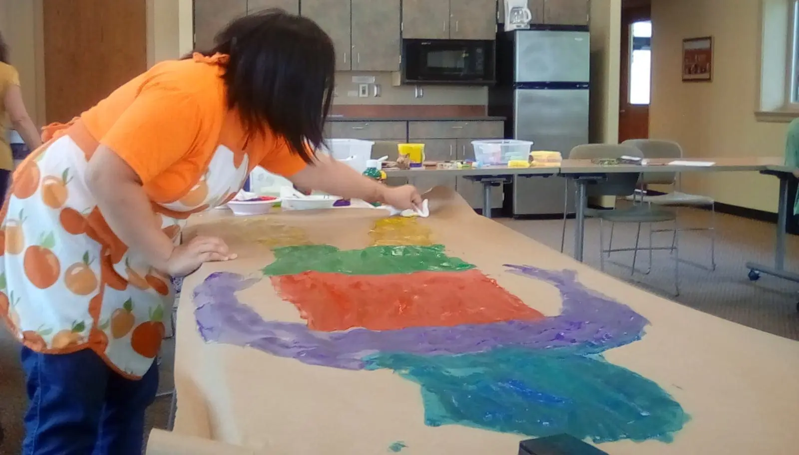 A person paints a colorful self-portrait on brown paper.