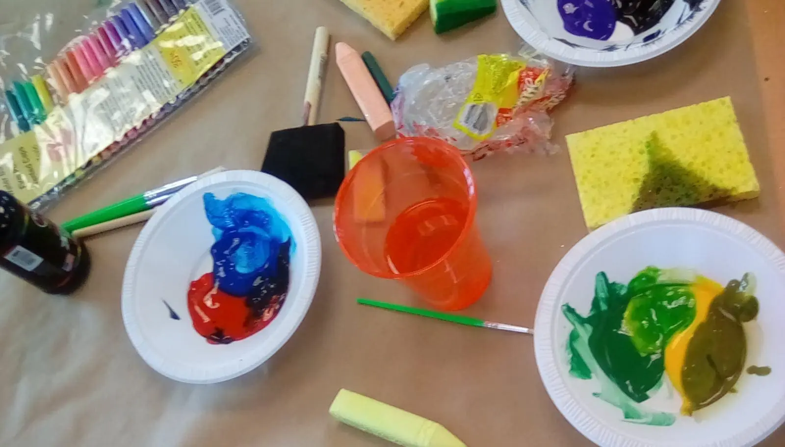 Art supplies including paints, brushes, sponges, and cups arranged on a surface.