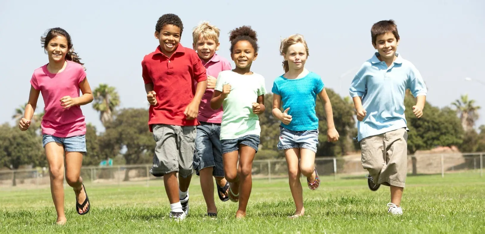 Group of children running in a grassy field on a sunny day.