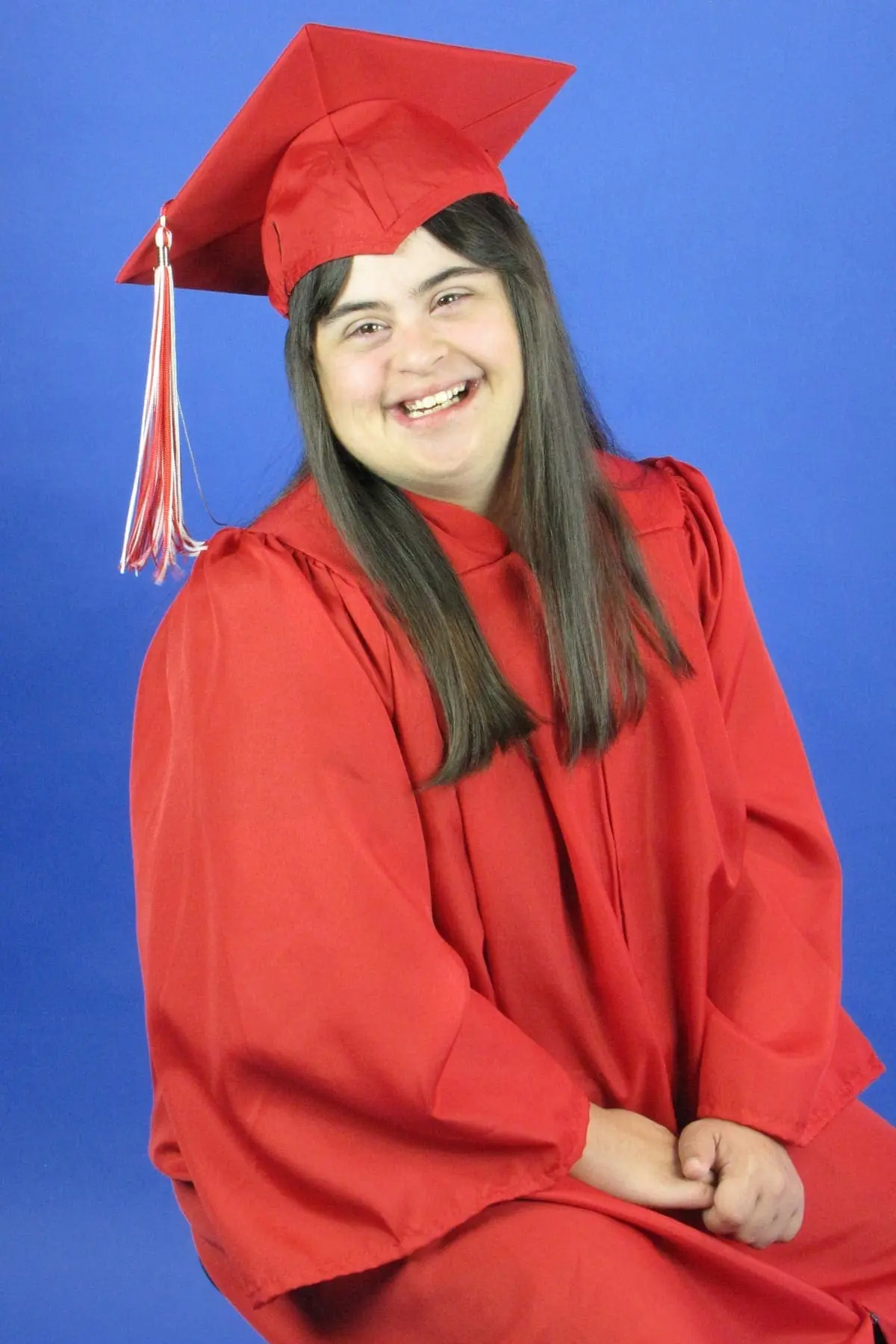 A young woman in a red graduation gown and cap smiles against a blue background.