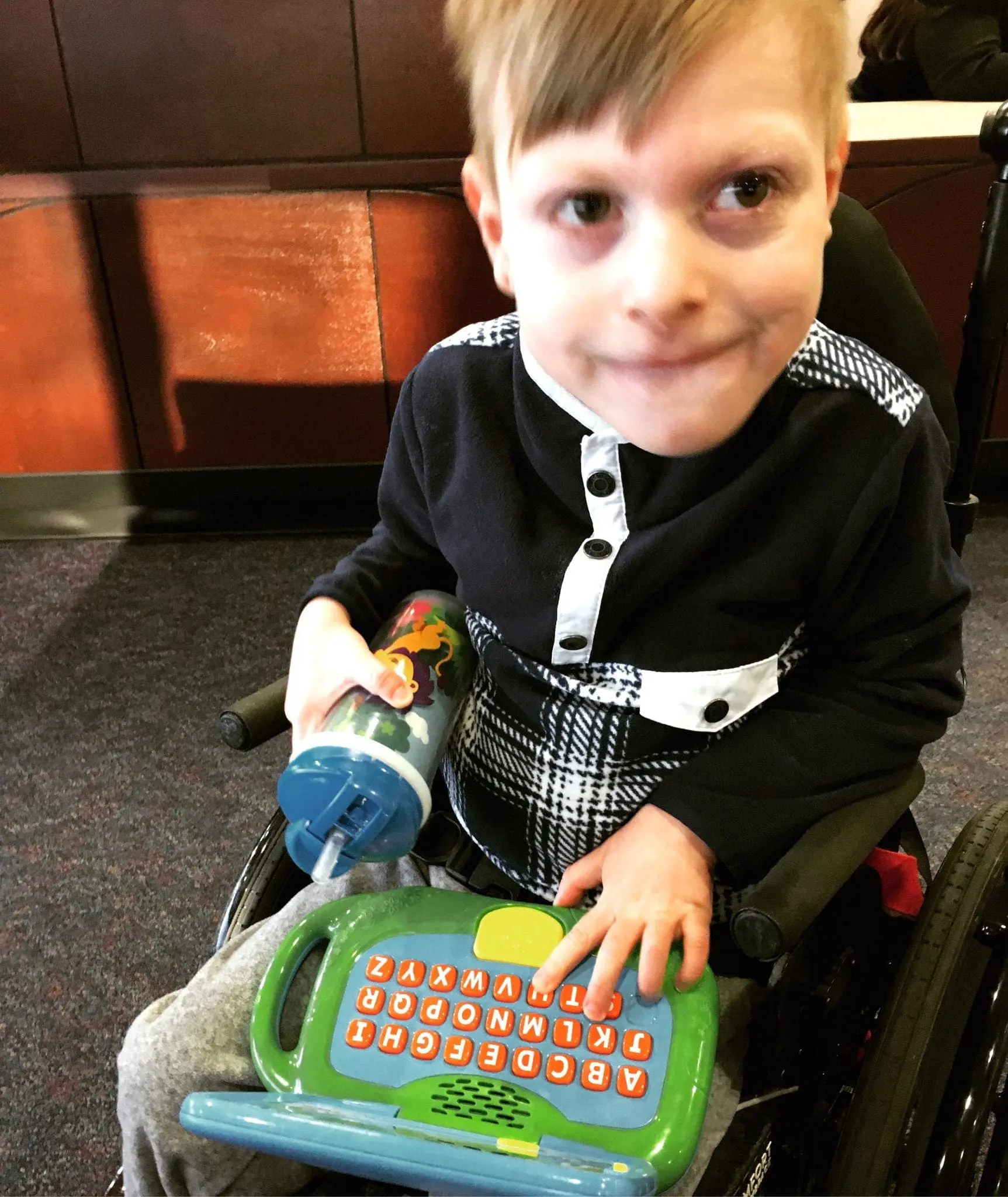 A young boy in a wheelchair uses a toy alphabet computer.