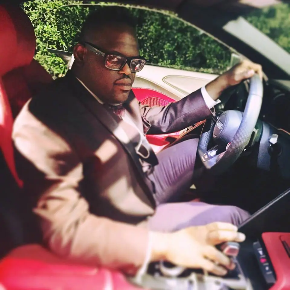Man wearing glasses and a suit driving a car.