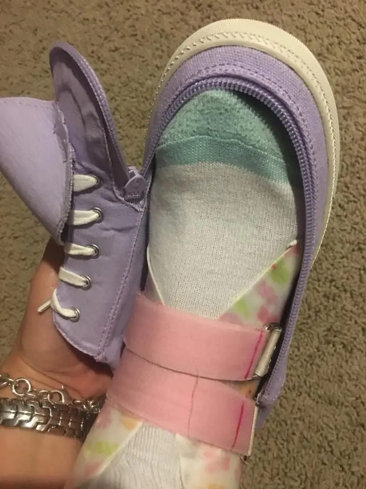 Close-up of a purple shoe with a zipper and pink straps, worn on a foot with a white sock.