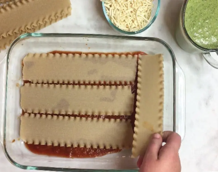 Lasagna noodles being layered into a baking dish with sauce.