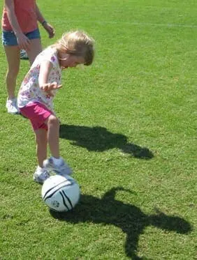 A young girl plays soccer with a ball on a green field.