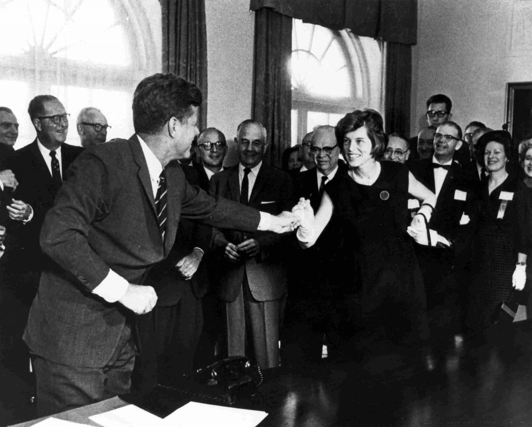 Eunice Kennedy Shriver shakes hands with President John F. Kennedy at a bill signing.