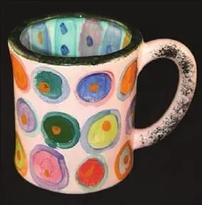 Pink ceramic mug with colorful circles painted on the outside and patterned inside.