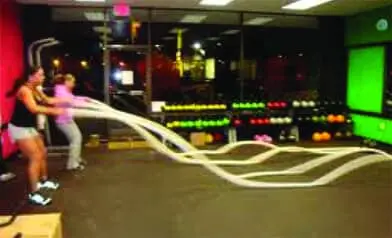 Two women using battle ropes in a gym.