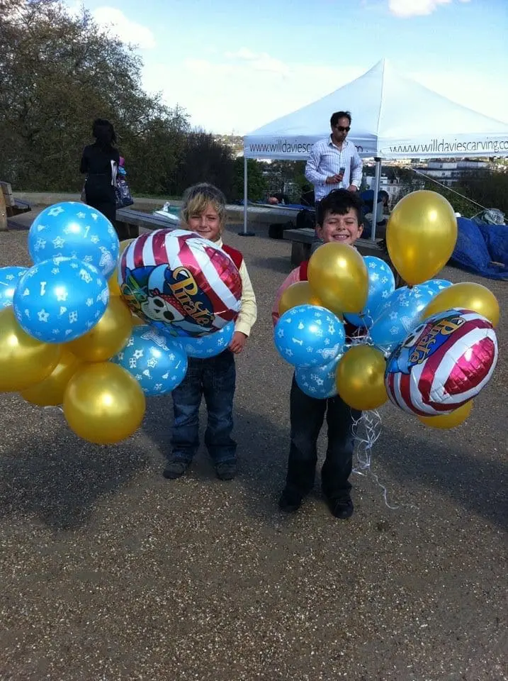 Two children stand holding balloons outside under a tent.