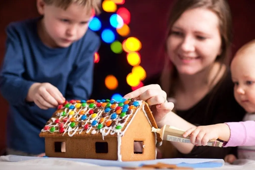 Woman and two children decorating a gingerbread house with colorful candies.