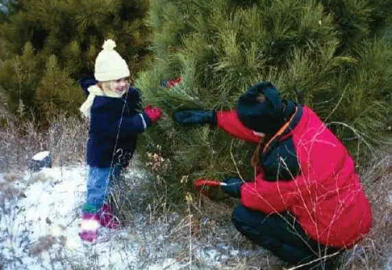 A woman in a red jacket and a child in a yellow hat examine a bush.