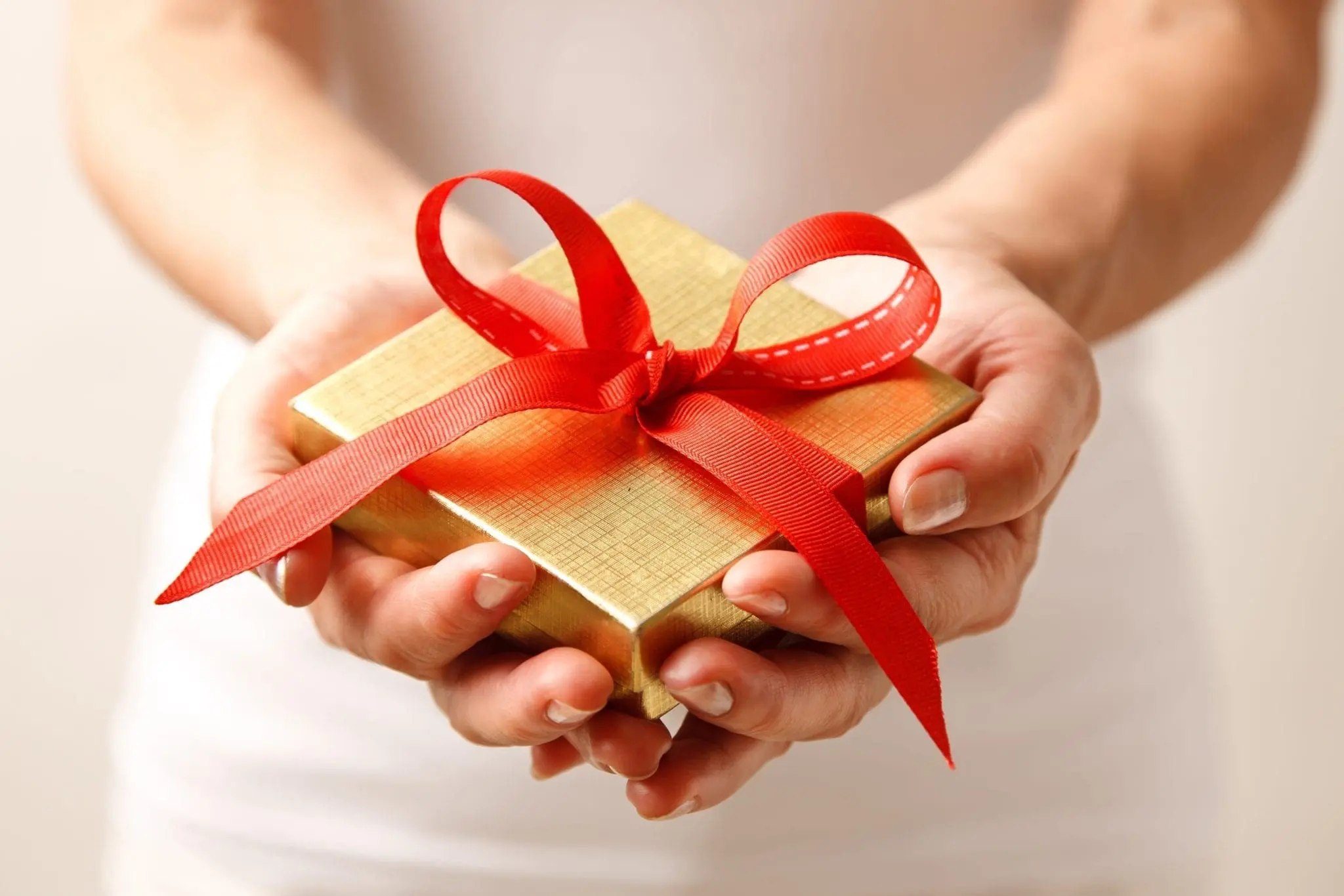 Hands holding a gold gift box tied with a red ribbon
