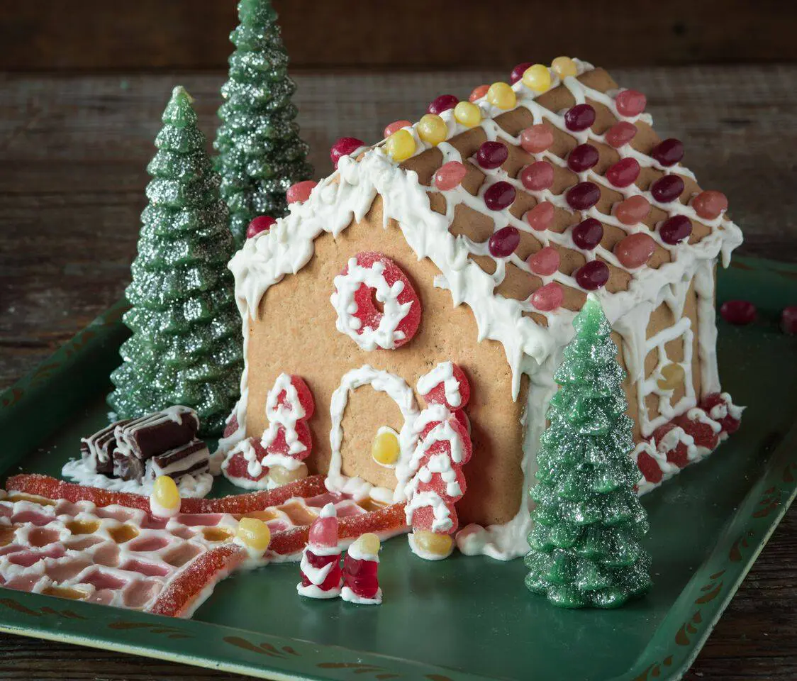 Gingerbread house decorated with icing, candy, and sugar-coated miniature trees on a green serving tray.