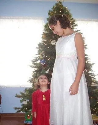 Two girls in dresses stand near a Christmas tree.