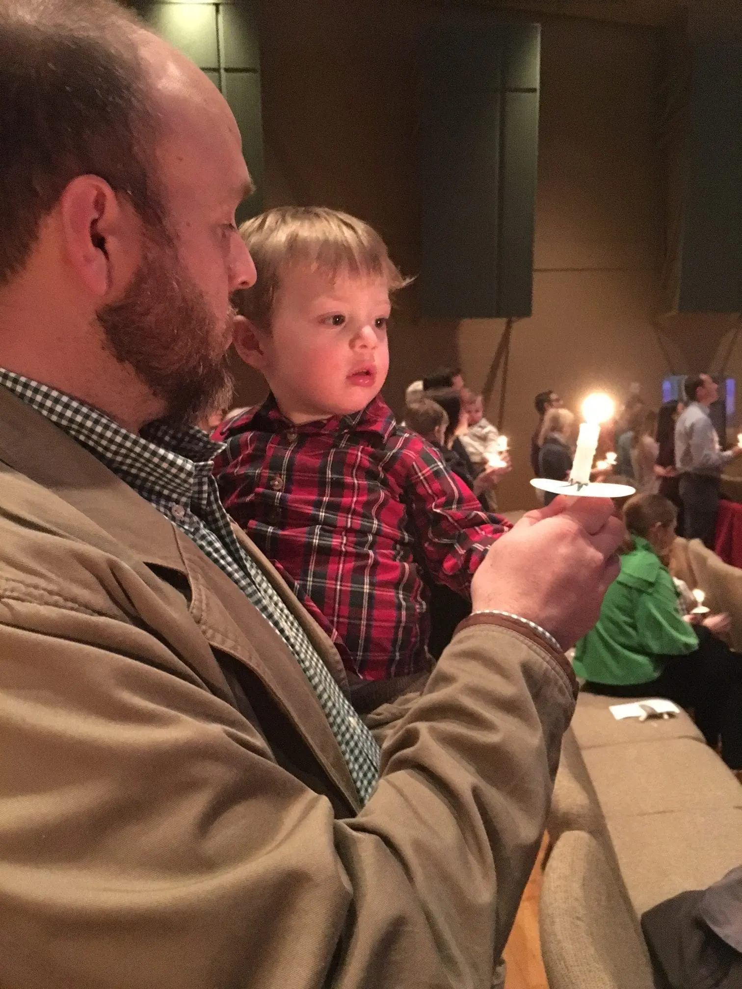 A man holds a young child who is looking at a lit candle.