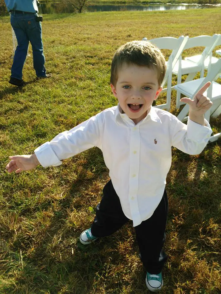 Young boy in a white shirt and dark pants playfully poses outdoors.