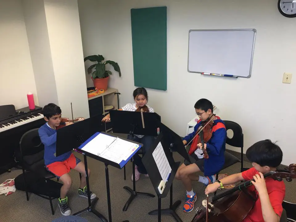 Four children practice string instruments in a music room.