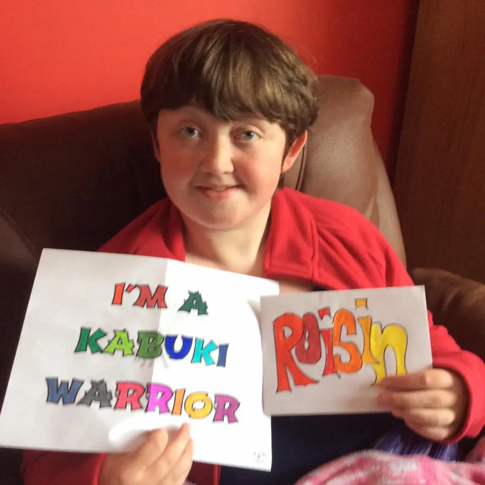Roisin holding signs that say "I'm a Kabuki Warrior" and her name.