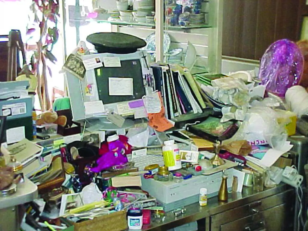 Cluttered desk with computer, papers, and various objects.