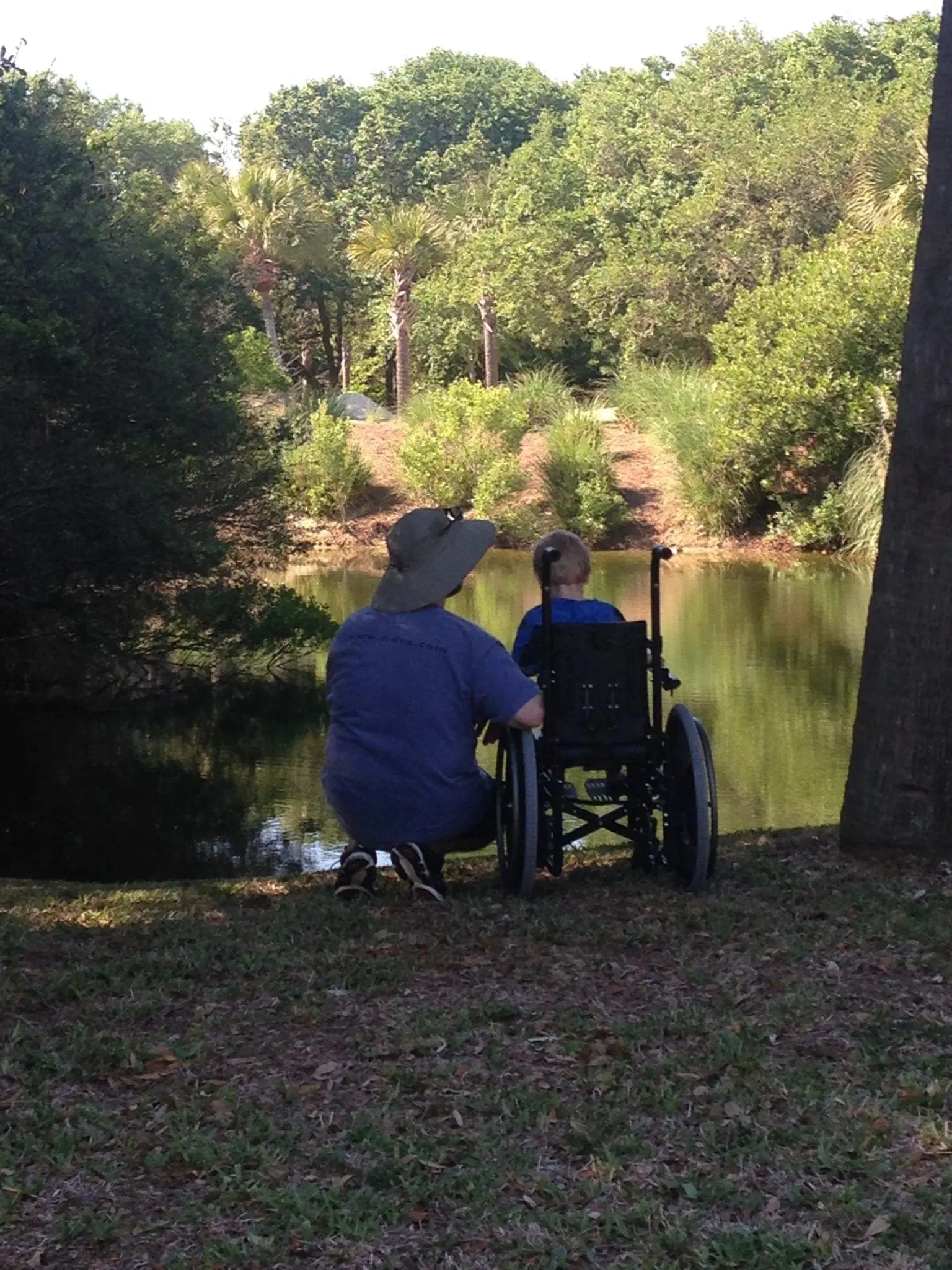 Person in wheelchair and another person by a lake.