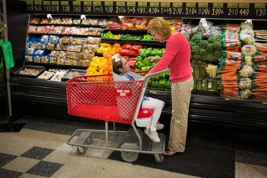 Woman pushes Caroline's Cart with a child in it down a grocery store aisle.