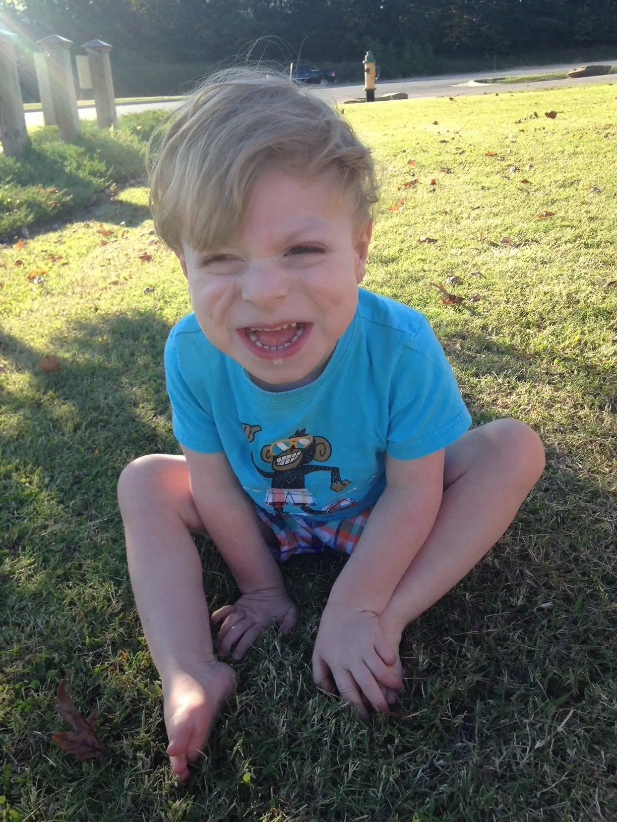 A young boy in a blue t-shirt sits on grass with his legs crossed.