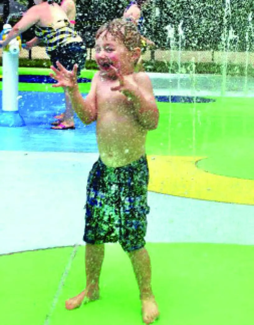 Seely, a young boy, laughs as he stands in a water park splash pad.