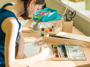 Young artist painting a picture at a table with art supplies.