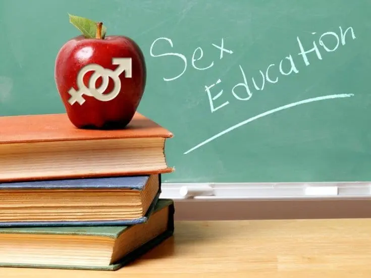 Apple with gender symbols on top of books in front of a chalkboard with "Sex Education" written on it