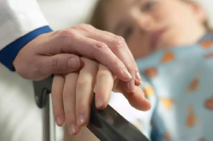 A medical professional holds a child's hand.