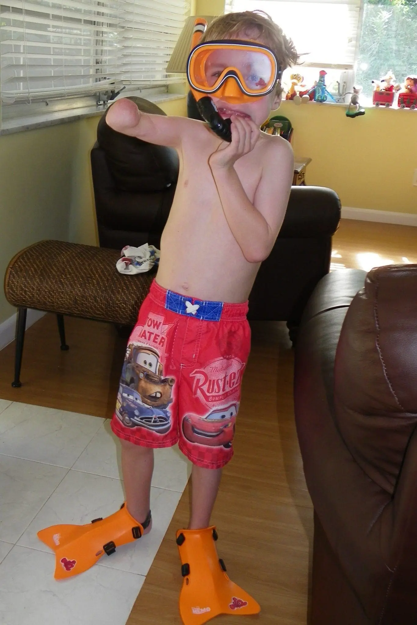 Boy in swim trunks, snorkel mask, and fins poses with hand to mouth.