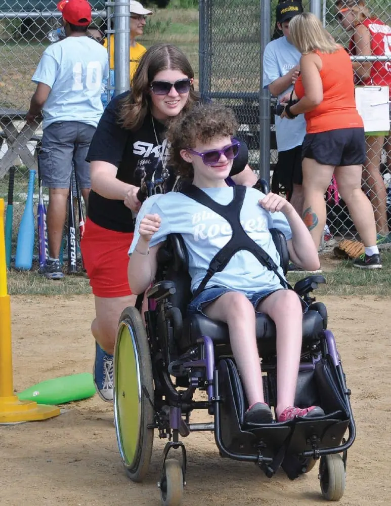 Allison pushing Cassidy in a wheelchair on a baseball field.