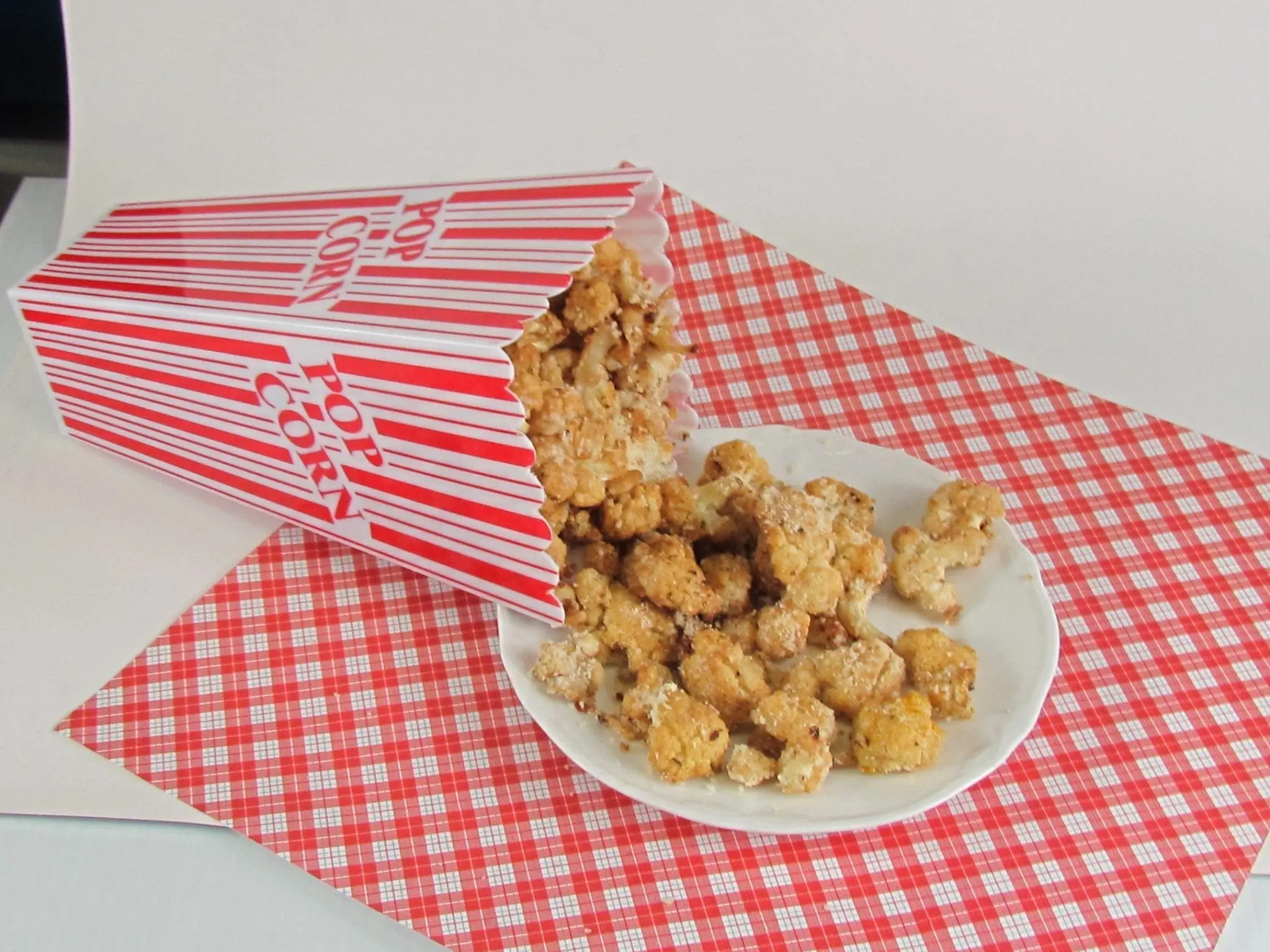 Cheesy cauliflower pieces spilling from a popcorn box onto a plate.
