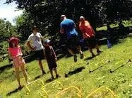 Four people, including two young adults and two children, participating in an outdoor exercise drill on a grassy slope.