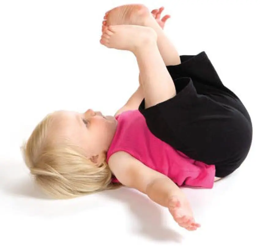 Child in a pink top and black pants lying on their back with knees bent and arms extended.