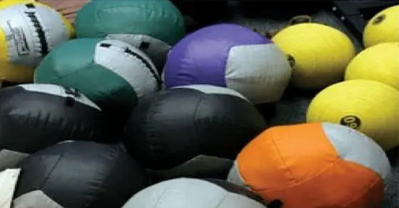 Several colorful medicine balls and sandbells are piled together.