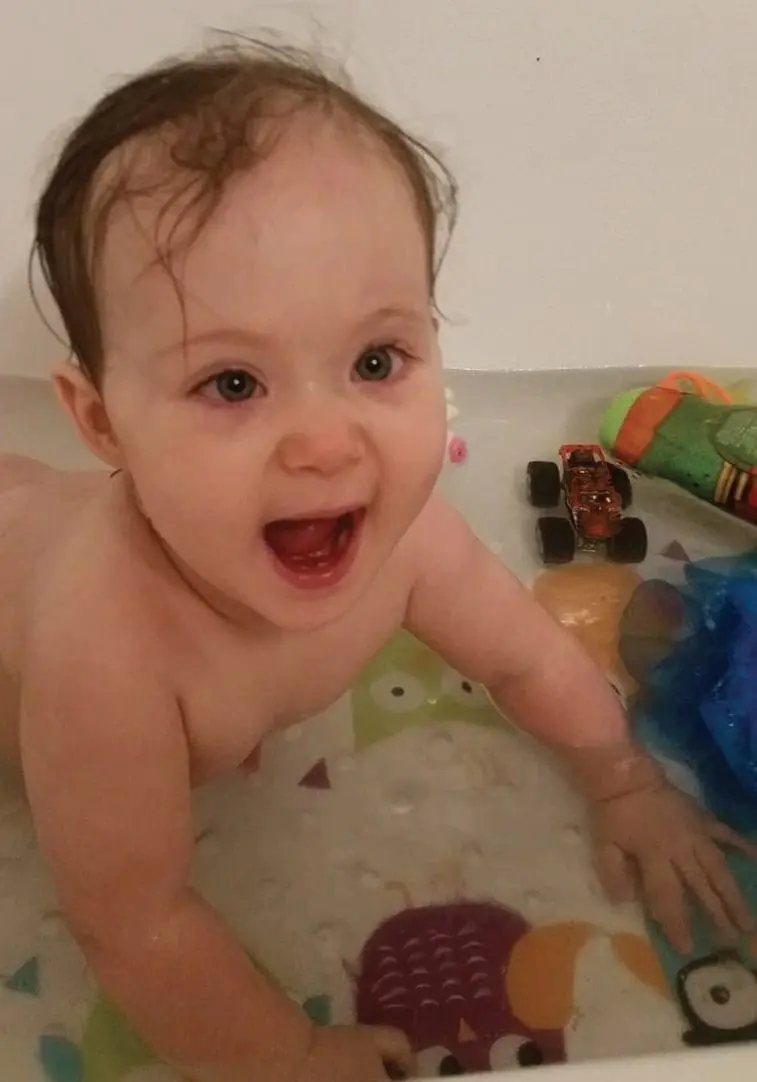 Baby in a bathtub with toys, smiling.