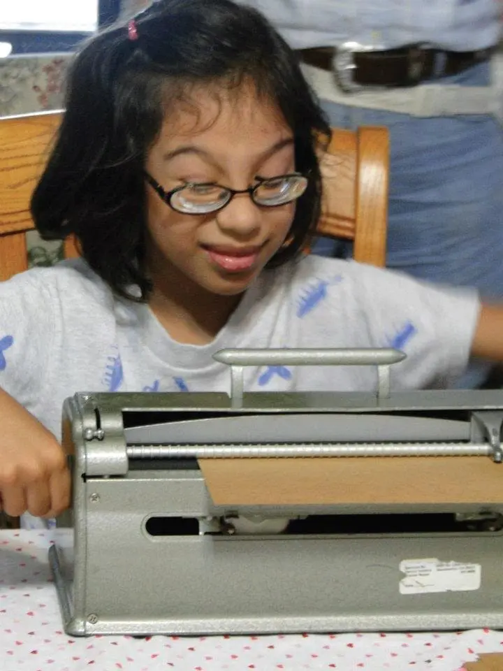 Young girl wearing glasses looking down at a braille writer.