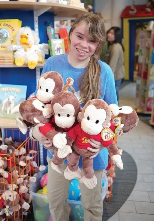 A young woman holds several stuffed monkeys in a store.