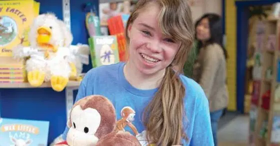 Young adult smiling while holding a stuffed animal in a bookstore.