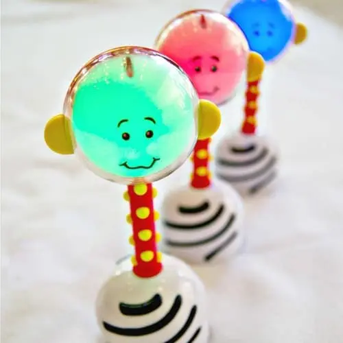 NogginStik toy glowing green with a smiling face, with other colorful NogginStiks in the background.