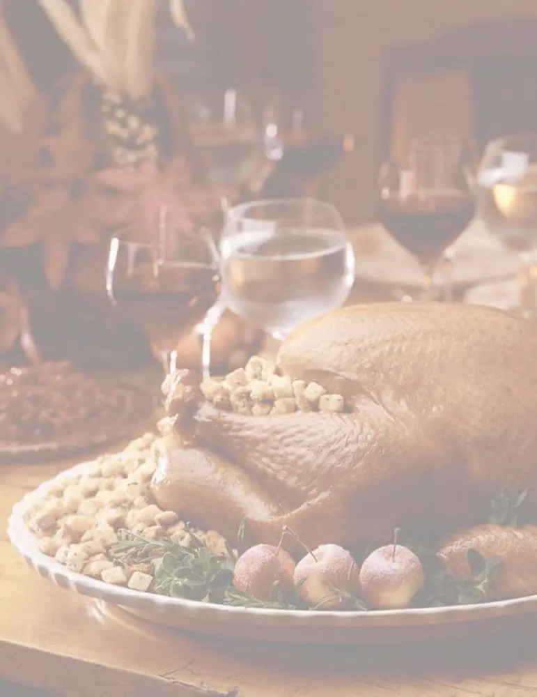 Roasted turkey garnished with apples and herbs on a holiday dinner table with glassware.