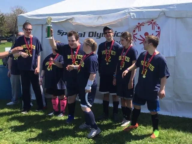Tom Petrik and a Special Olympics soccer team celebrate with a trophy.